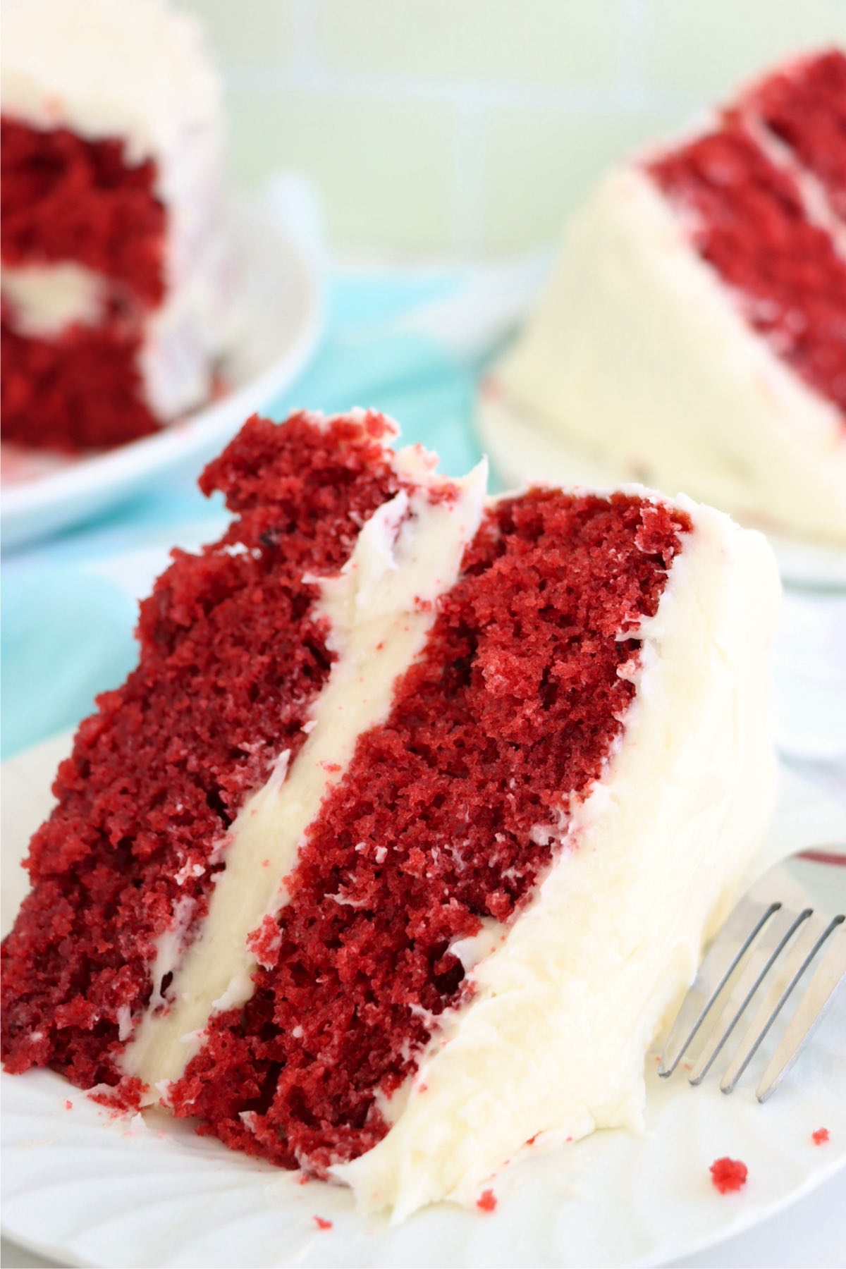 A beautifully sliced red velvet cake, featuring two layers of soft, vibrant red cake filled with creamy frosting, served on a white plate.