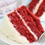 A wide shot of a slice of red velvet cake, capturing the contrast between the vivid red layers and the white frosting, with crumbs scattered on the plate.