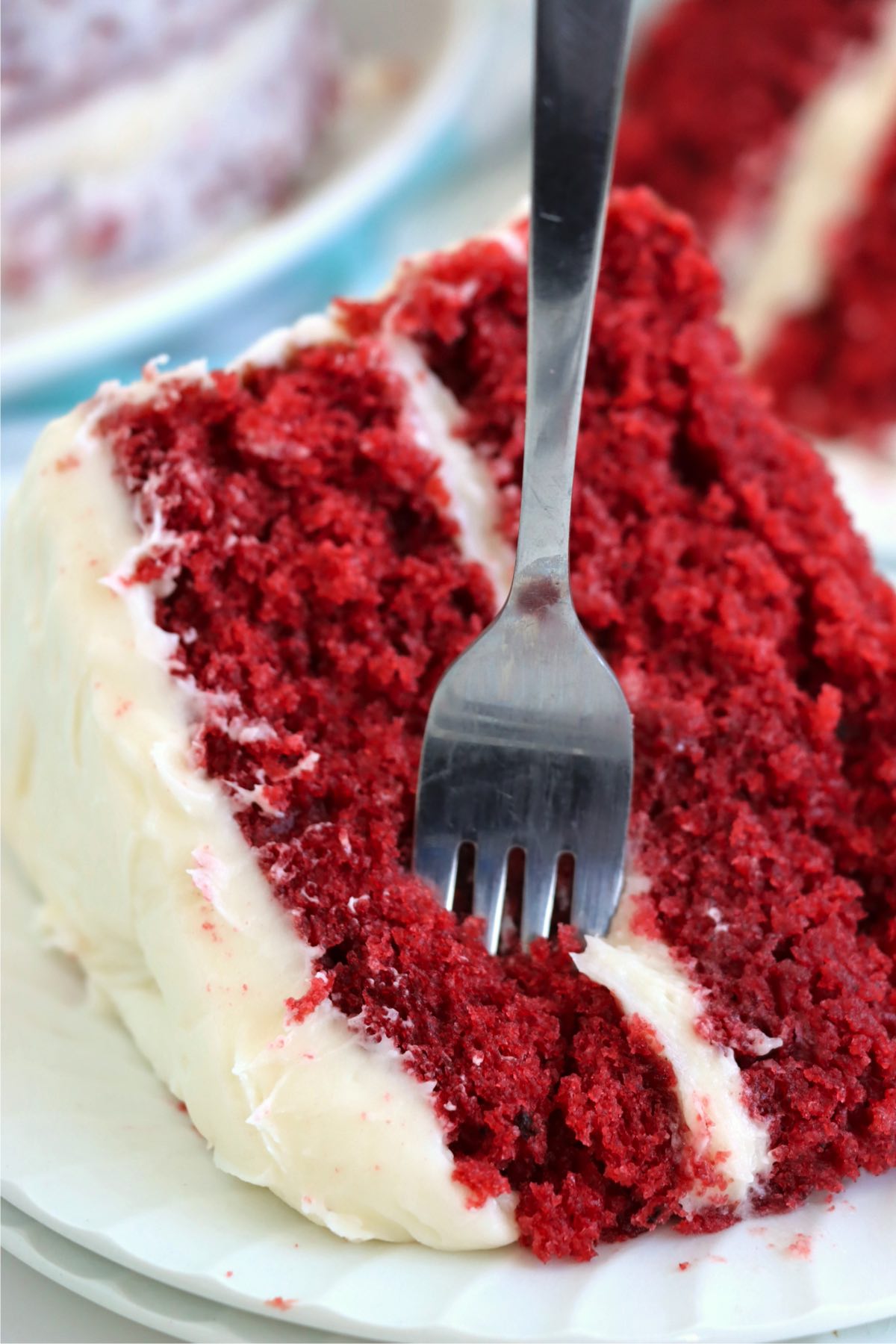 A fork breaking into a piece of red velvet cake, emphasizing the cake’s soft, moist texture and creamy frosting layers.