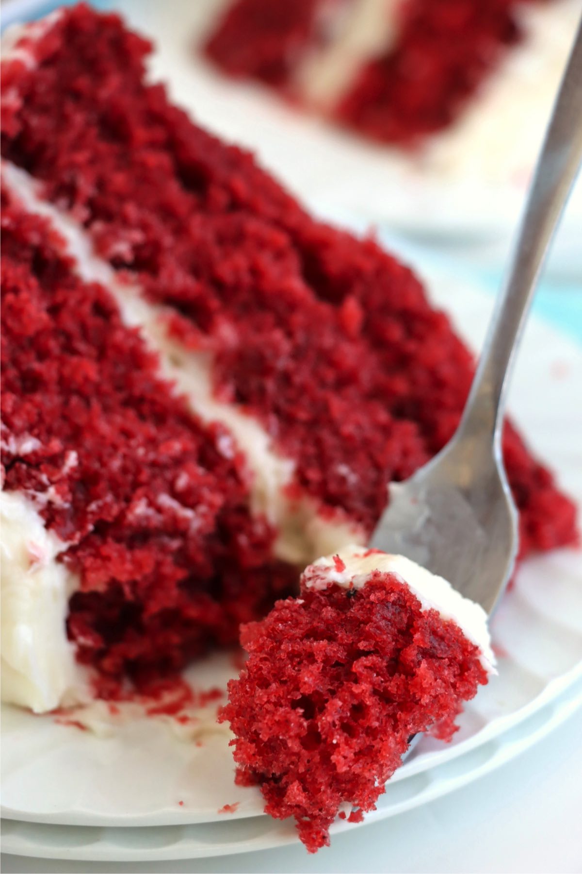 A fork lifting a bite of red velvet cake, showcasing the fluffy red crumb and smooth frosting for a mouthwatering view.