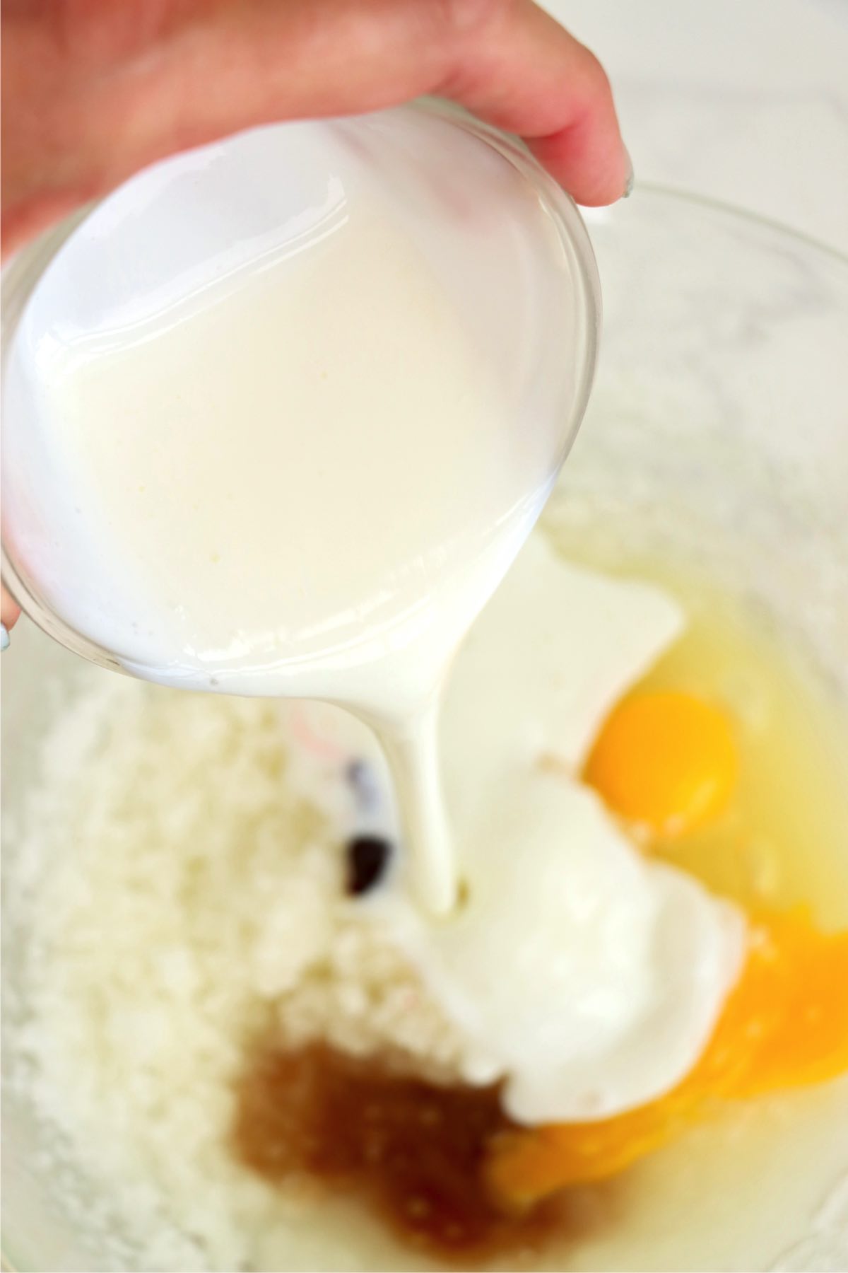 A creamy mixture of buttermilk, eggs, and vanilla extract being poured into a bowl containing other liquid ingredients, capturing the richness and consistency of the batter.