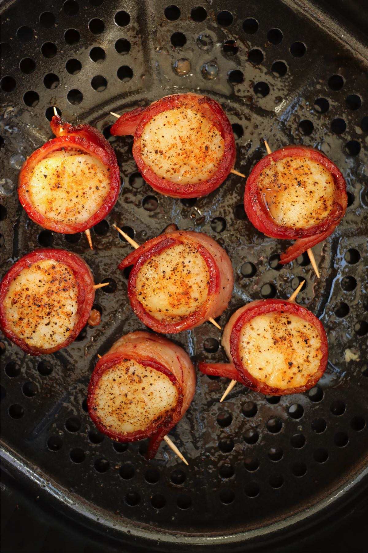 Golden brown bacon-wrapped scallops rest in the air fryer basket, with crispy edges and a caramelized glaze.