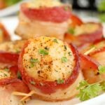 Perfectly cooked scallops wrapped in crispy bacon, served on a white plate with a garnish of parsley.