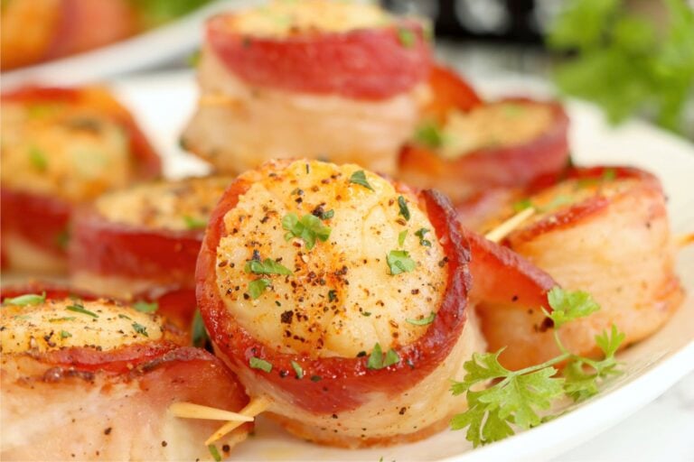 Perfectly cooked scallops wrapped in crispy bacon, served on a white plate with a garnish of parsley.