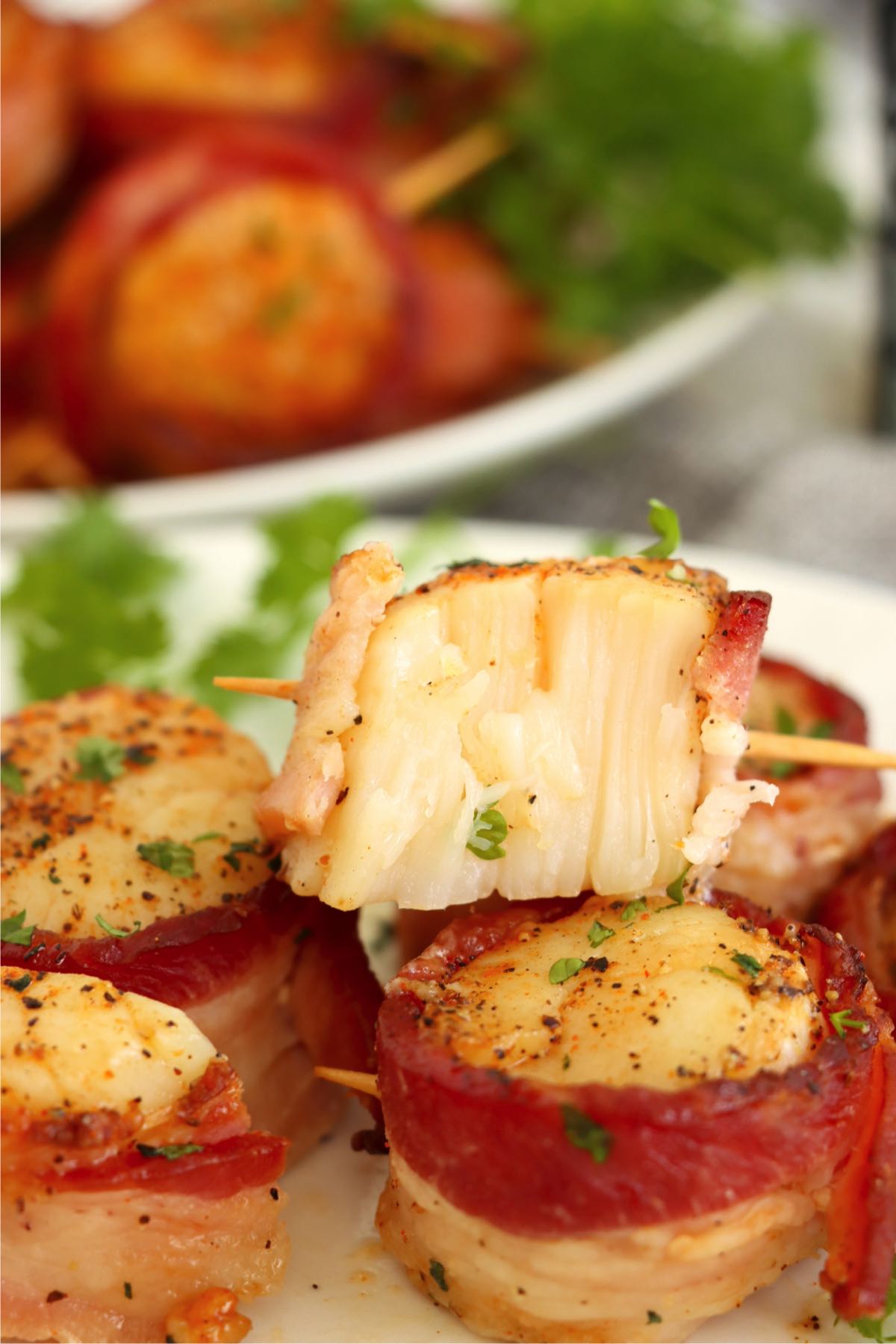 A scallop wrapped in crispy bacon is cut in half, revealing its tender, flaky interior, ready to be enjoyed.