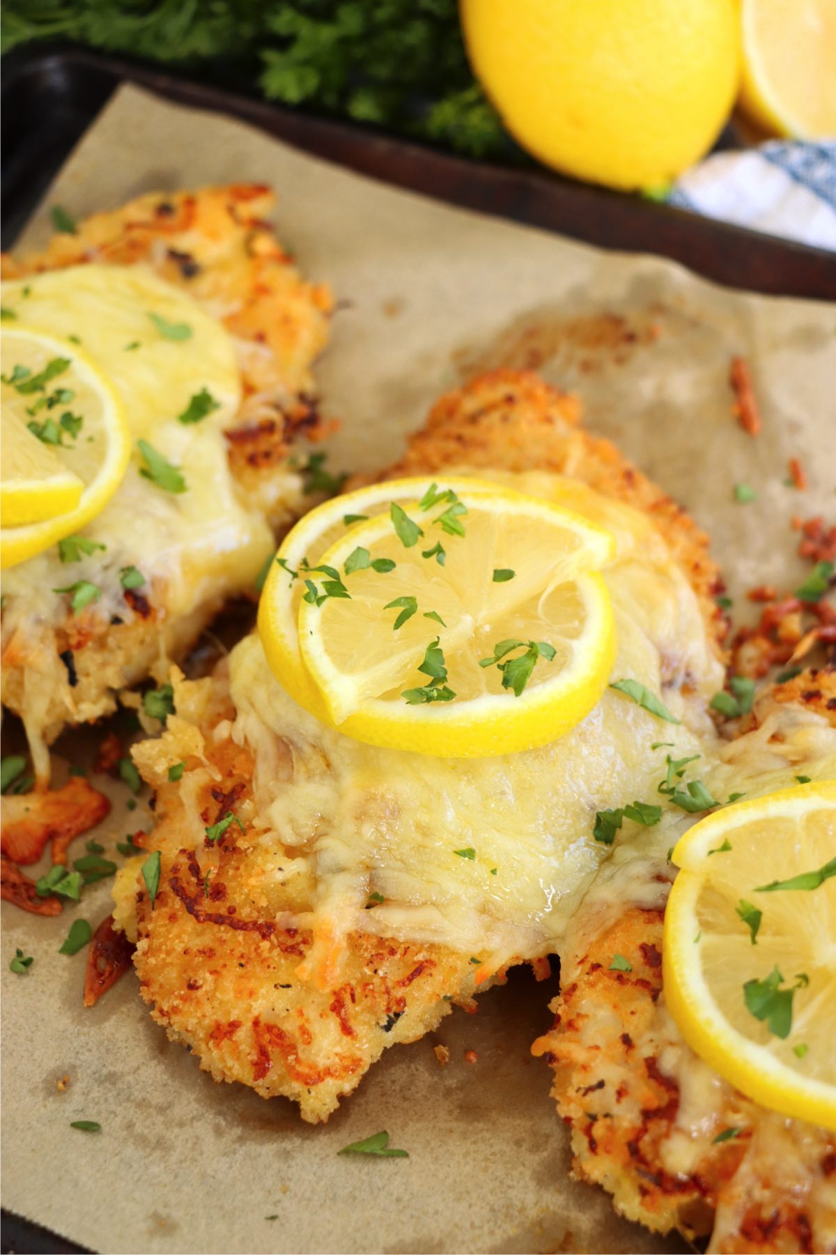 Freshly baked Lemon Chicken Romano, featuring golden, crispy breading, melted cheese, and bright lemon slices, garnished with chopped parsley for a vibrant finish.