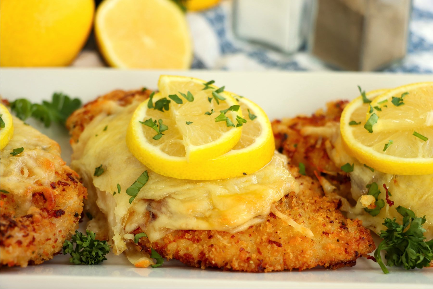 A plated Lemon Chicken Romano with crispy breading, melted cheese, fresh parsley, and lemon slices for a bright finish.