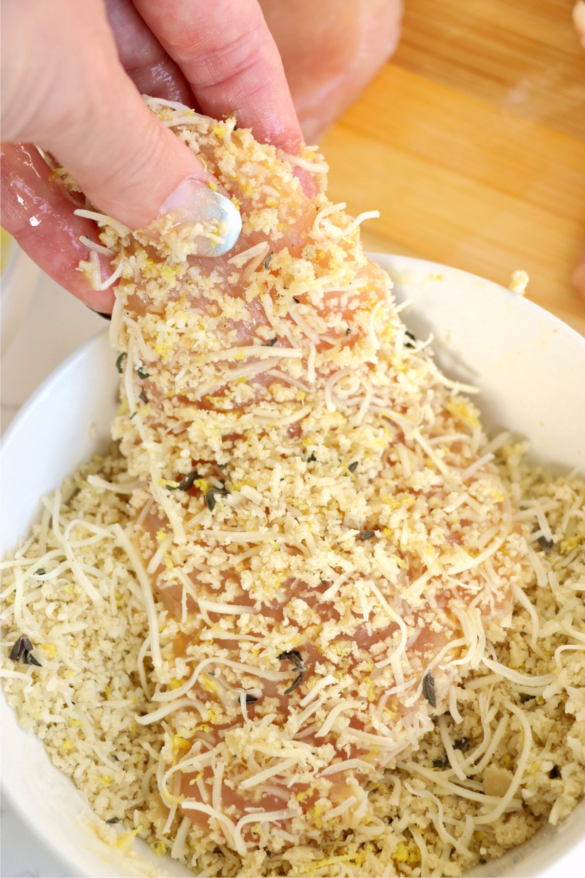 Hand pressing a chicken breast into the breadcrumb and cheese mixture, ensuring an even coating for a crispy texture.