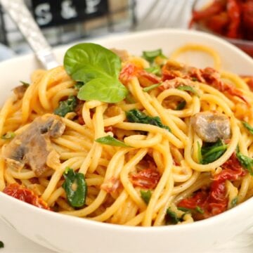 Pasta and sun-dried tomatoes in a white bowl garnished with basil.