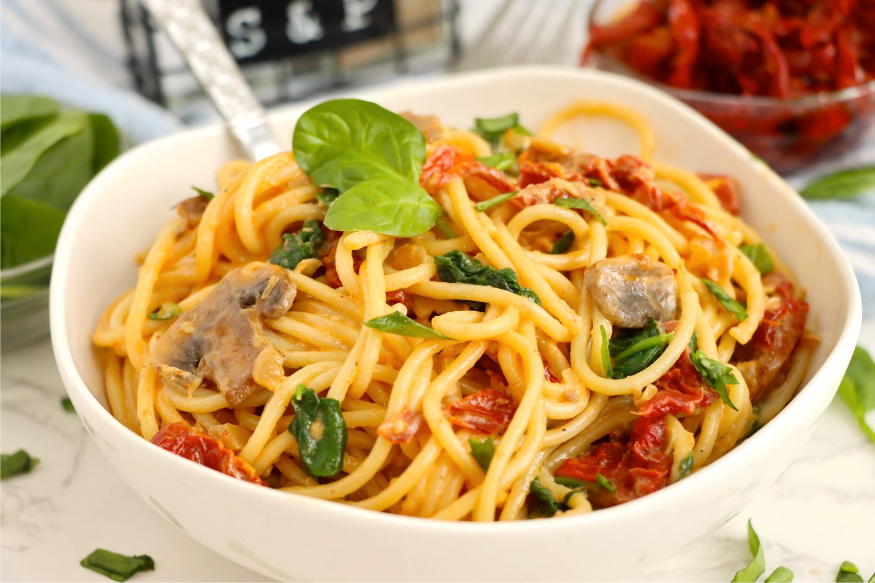 Pasta and sun-dried tomatoes in a white bowl garnished with basil.