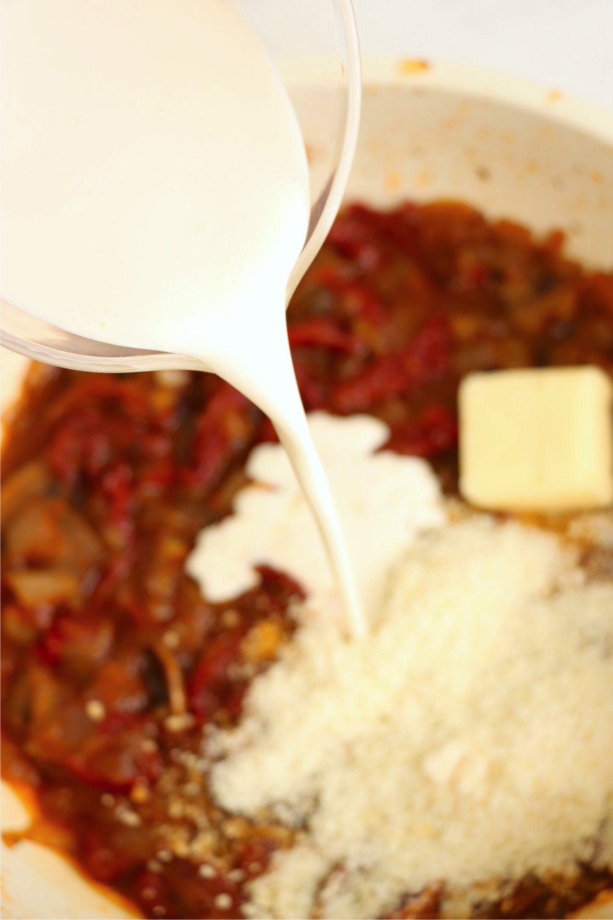 Heavy cream and Parmesan cheese being poured into a skillet, combining with vegetables to form a rich, creamy sauce.