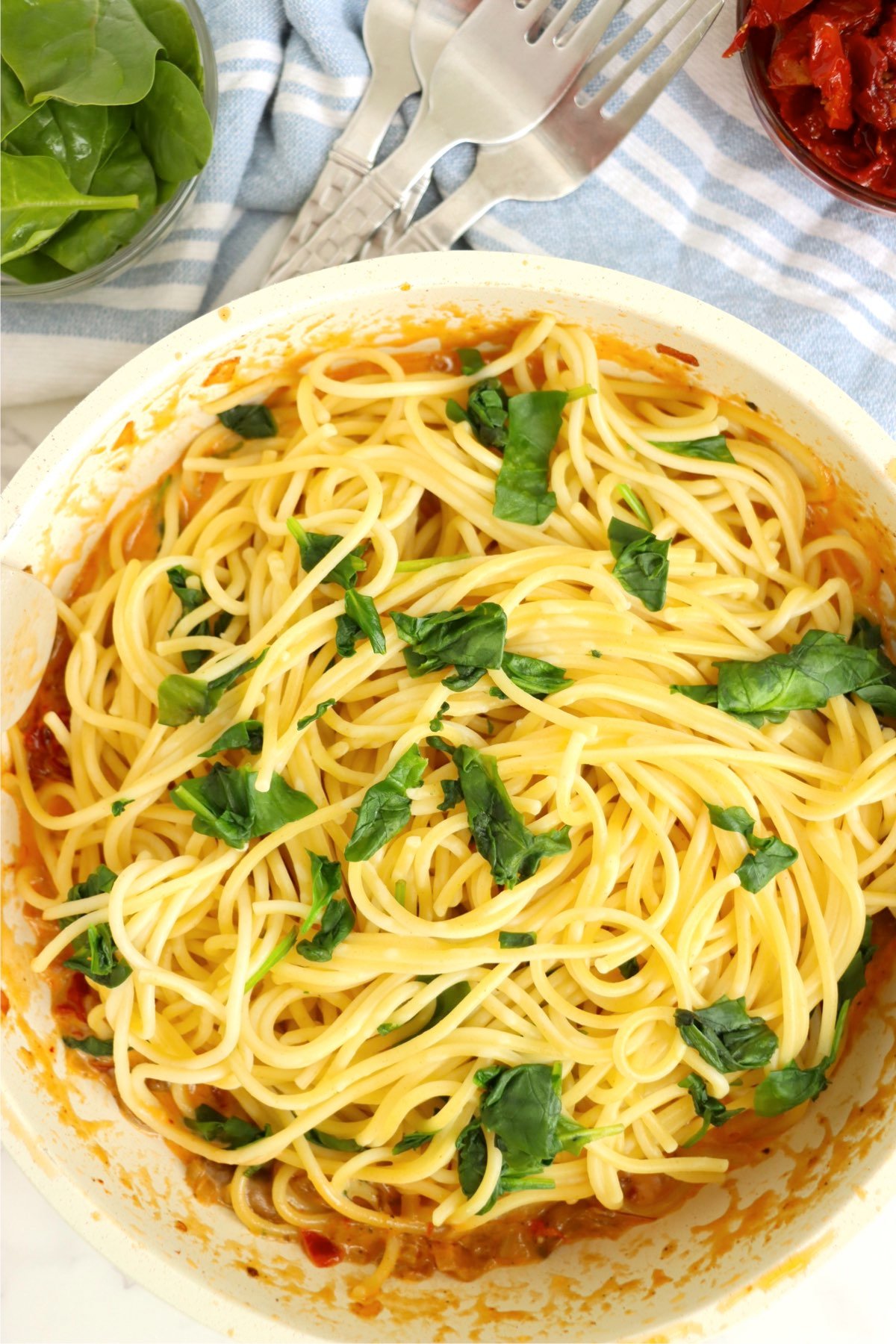 Creamy pasta, topped with fresh spinach, mixed in a skillet.