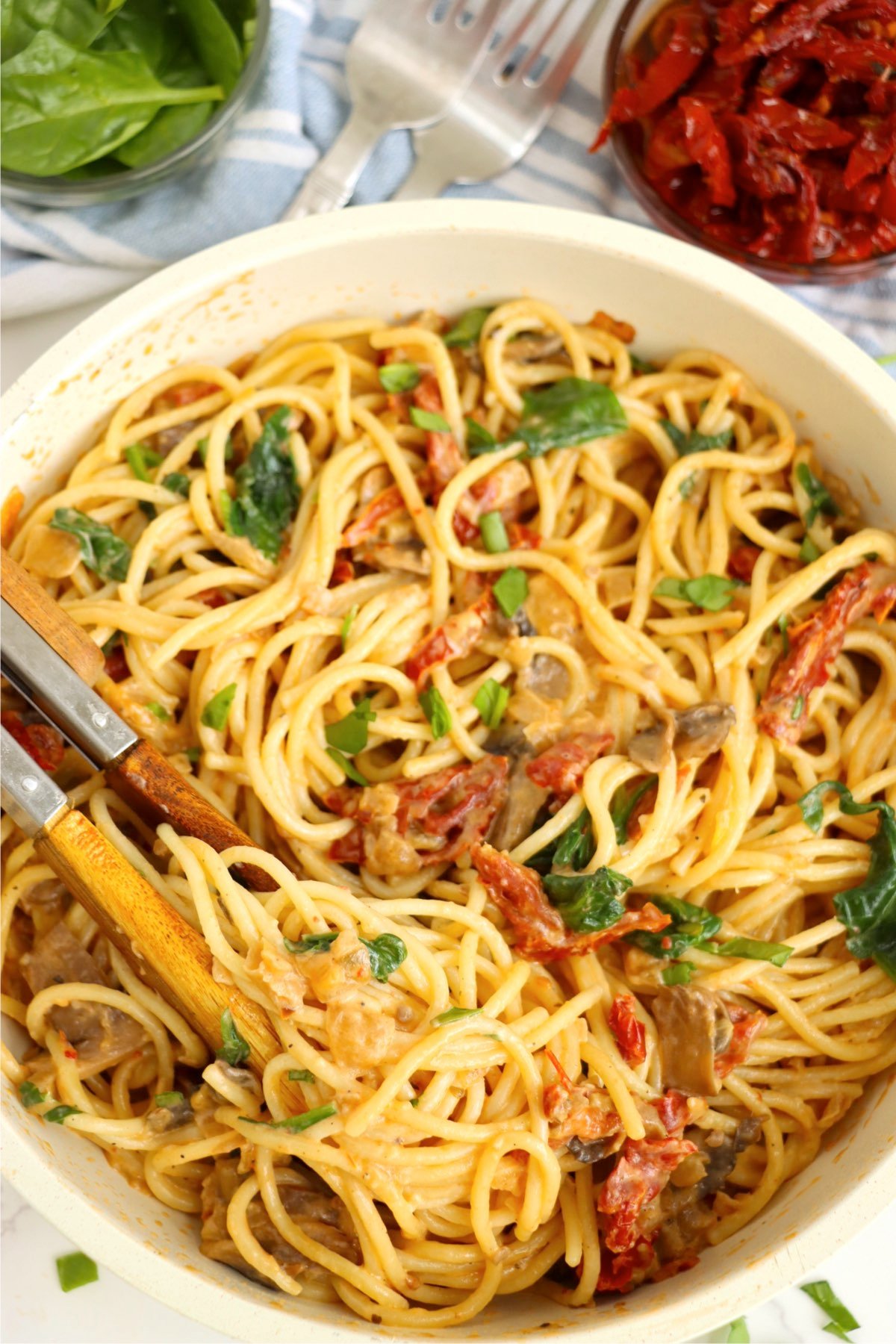 A creamy spinach and sun-dried tomato pasta in a skillet, tossed with spaghetti, mushrooms, and a Parmesan-infused sauce, ready to be served.