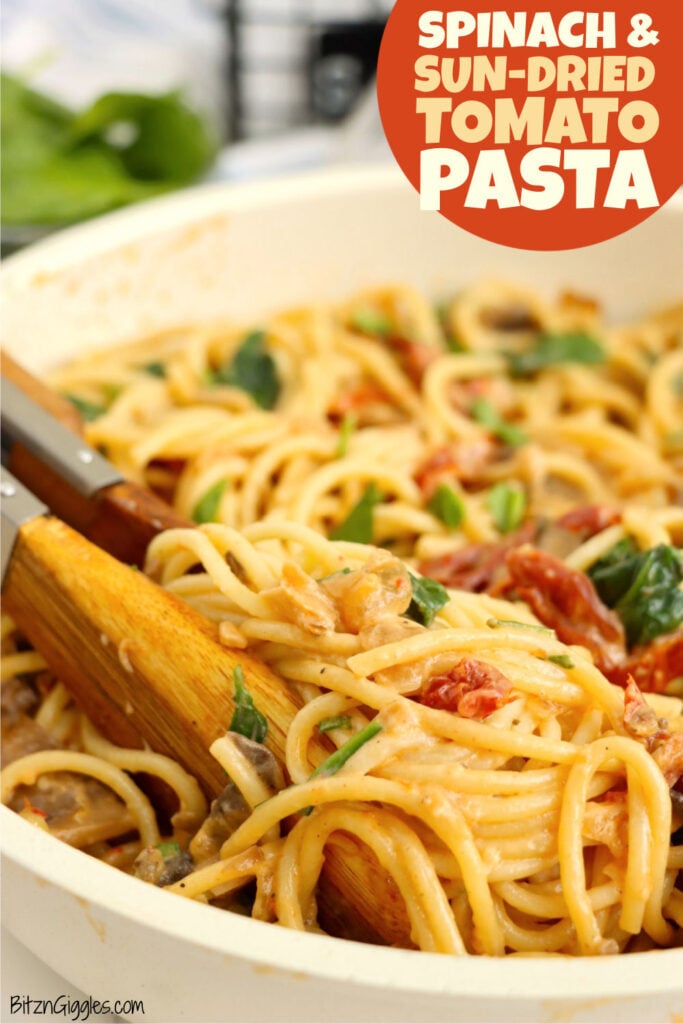 A tongs grabbing hold of sun-dried tomato pasta in a large white serving bowl.