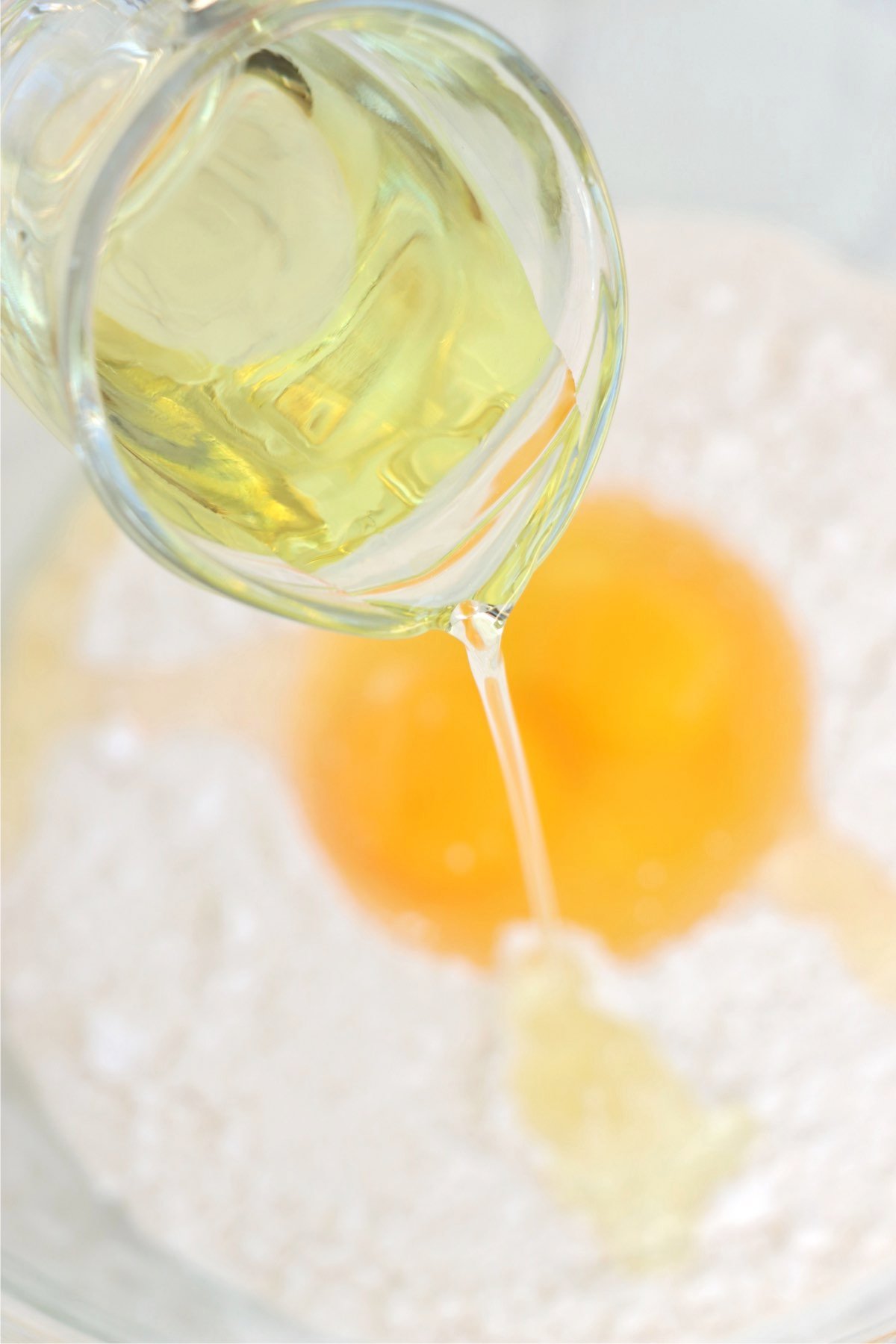 Vegetable oil being poured into a bowl containing eggs and cake mix, capturing the start of the cookie dough mixing process.