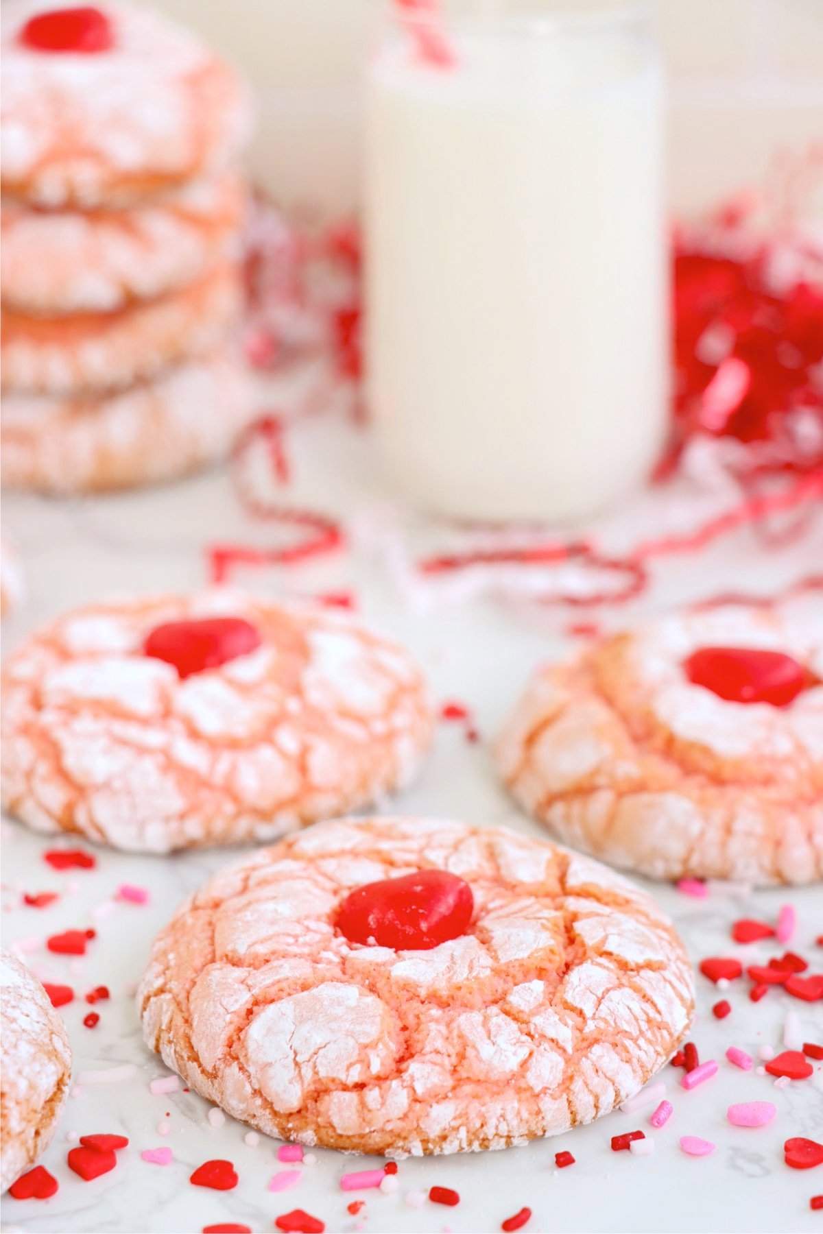 Strawberry crinkle cookies displayed with a glass of milk, surrounded by festive heart-shaped sprinkles.