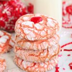 A stack of strawberry crinkle cookies topped with a red candy heart, paired with a glass of milk.