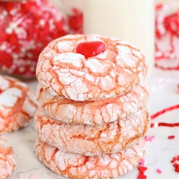 A stack of strawberry crinkle cookies topped with a red candy heart, paired with a glass of milk.