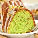 A single slice of pistachio bundt cake on a white plate, showing its vibrant green interior and nutty texture.