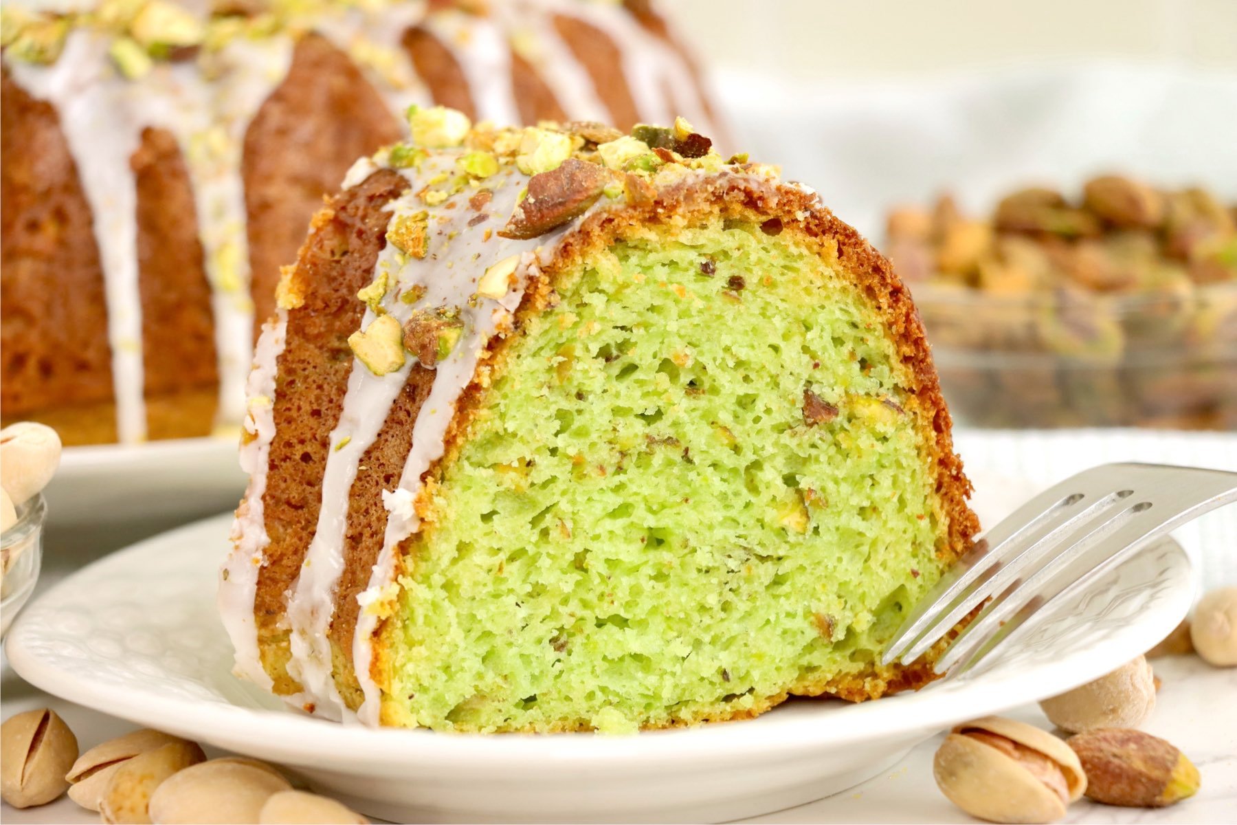 A single slice of pistachio bundt cake on a white plate, showing its vibrant green interior and nutty texture.