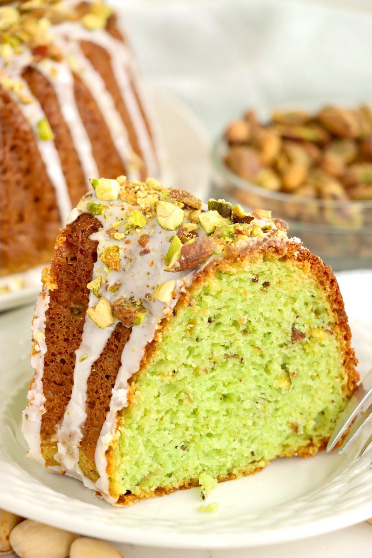 A fork beside a slice of pistachio bundt cake, highlighting its soft crumb and pistachio-studded interior.