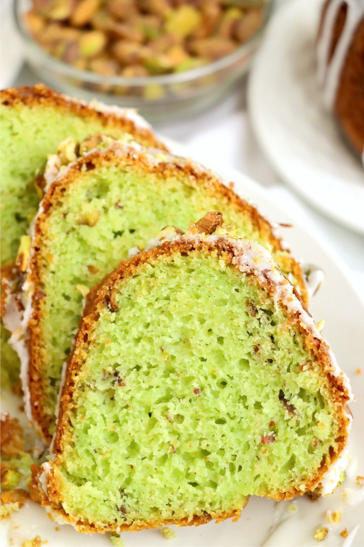 Several slices of pistachio bundt cake arranged on a plate, displaying the cake’s moist green center and golden crust.