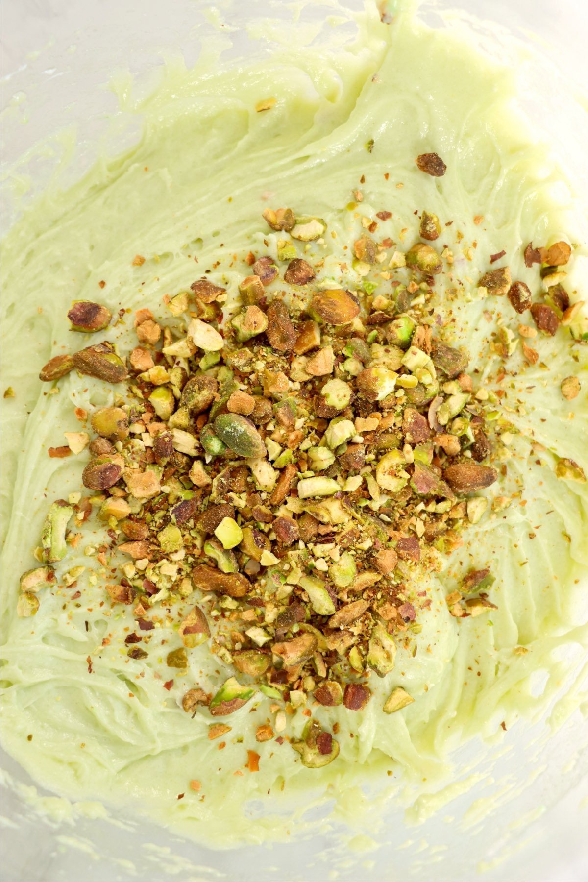 A thick, pale green cake batter in a bowl with freshly chopped pistachios sprinkled on top.