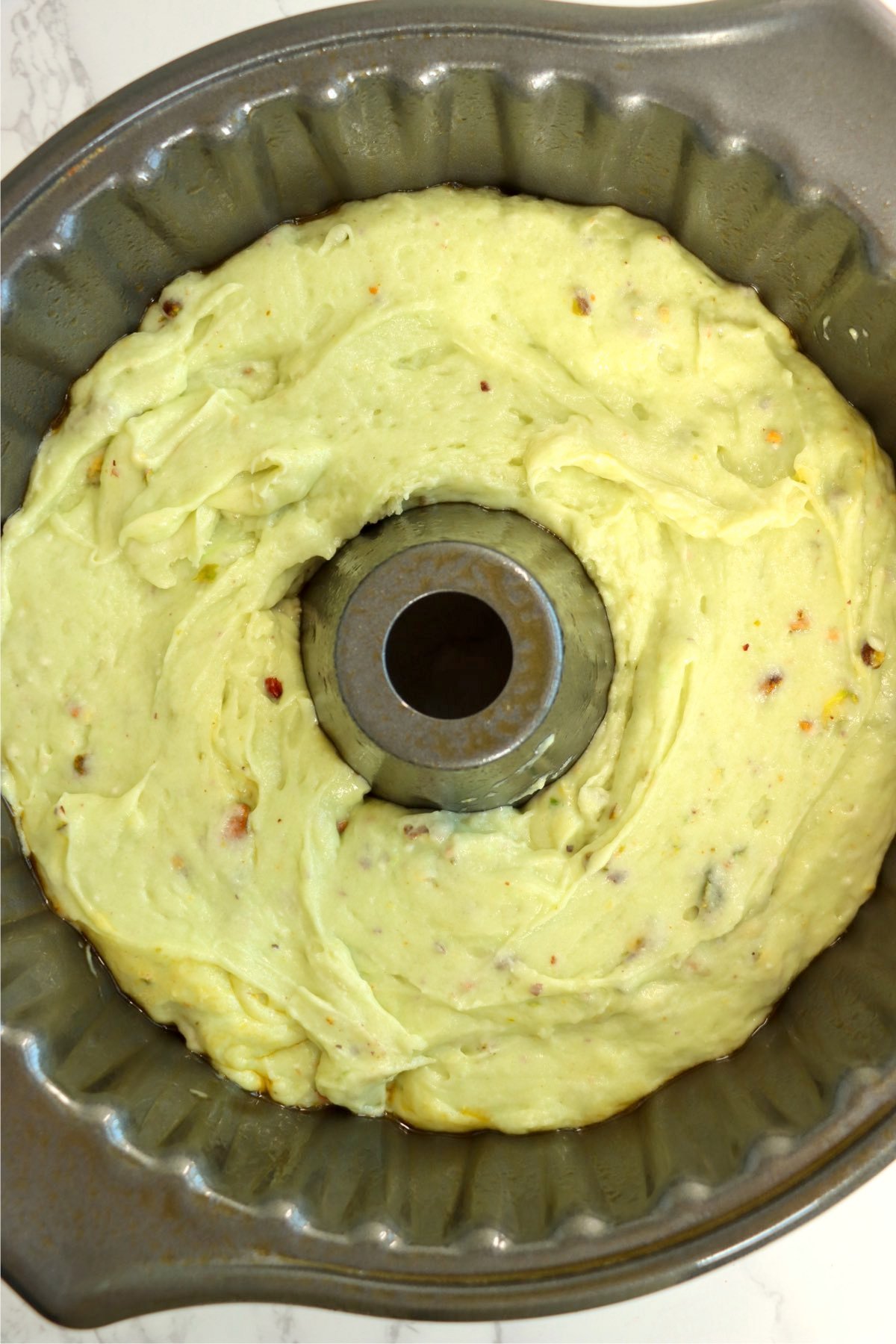 A bundt cake pan filled with smooth, green pistachio cake batter, evenly spread around the ring.