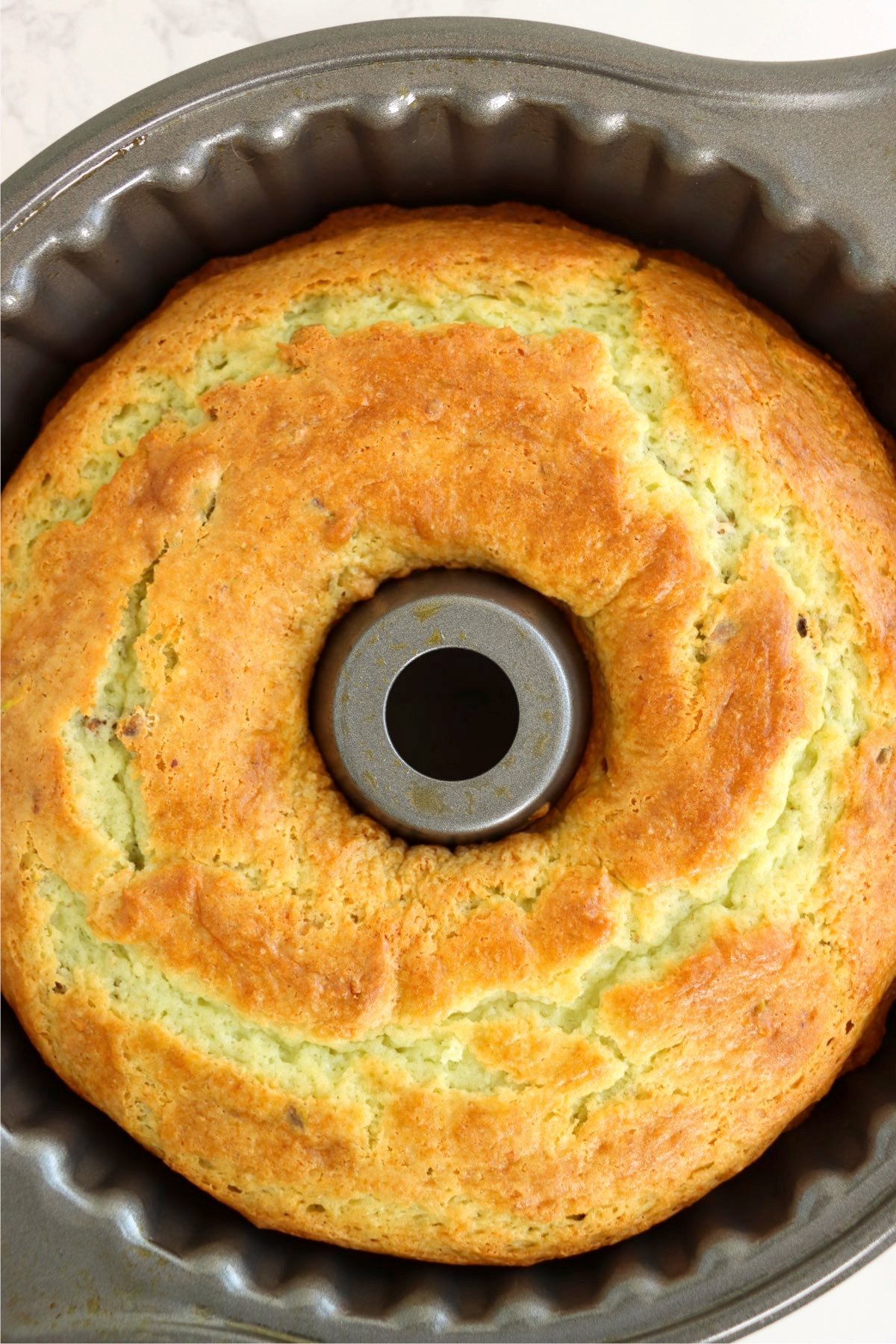 A freshly baked bundt cake with a golden-brown crust, still in the pan, showing a slightly cracked top.