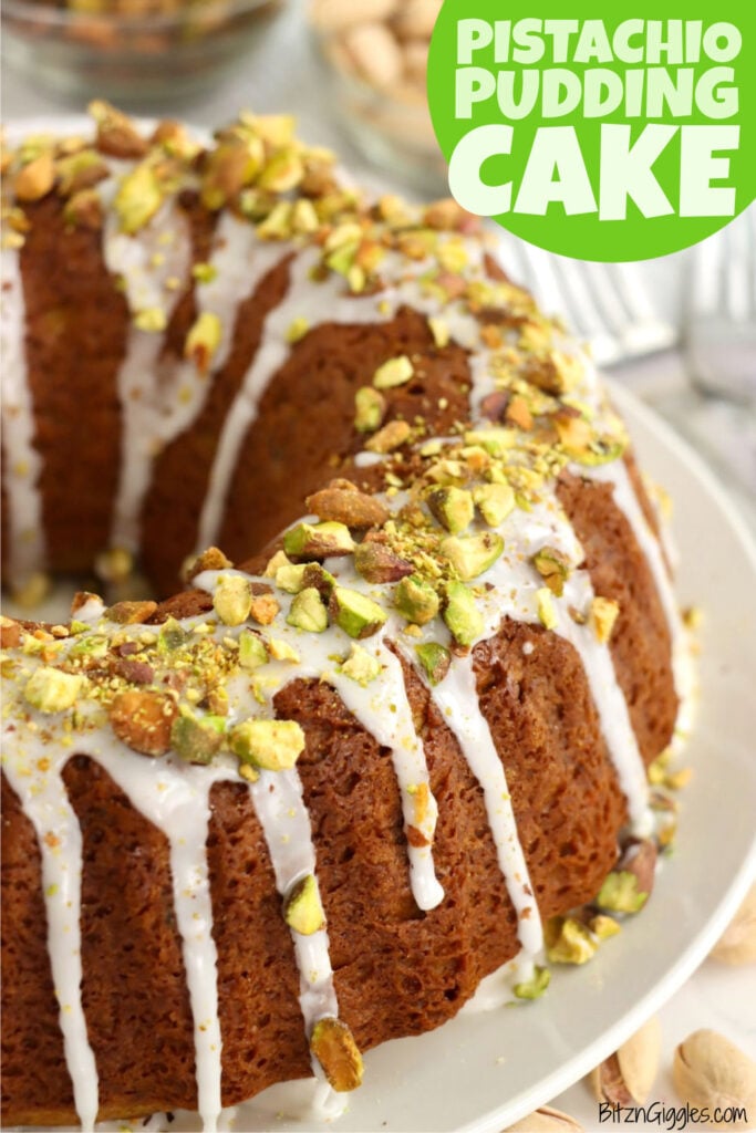 A close-up of a golden brown bundt cake drizzled with white glaze and topped with chopped pistachios, sitting on a white plate with whole pistachios in the background.