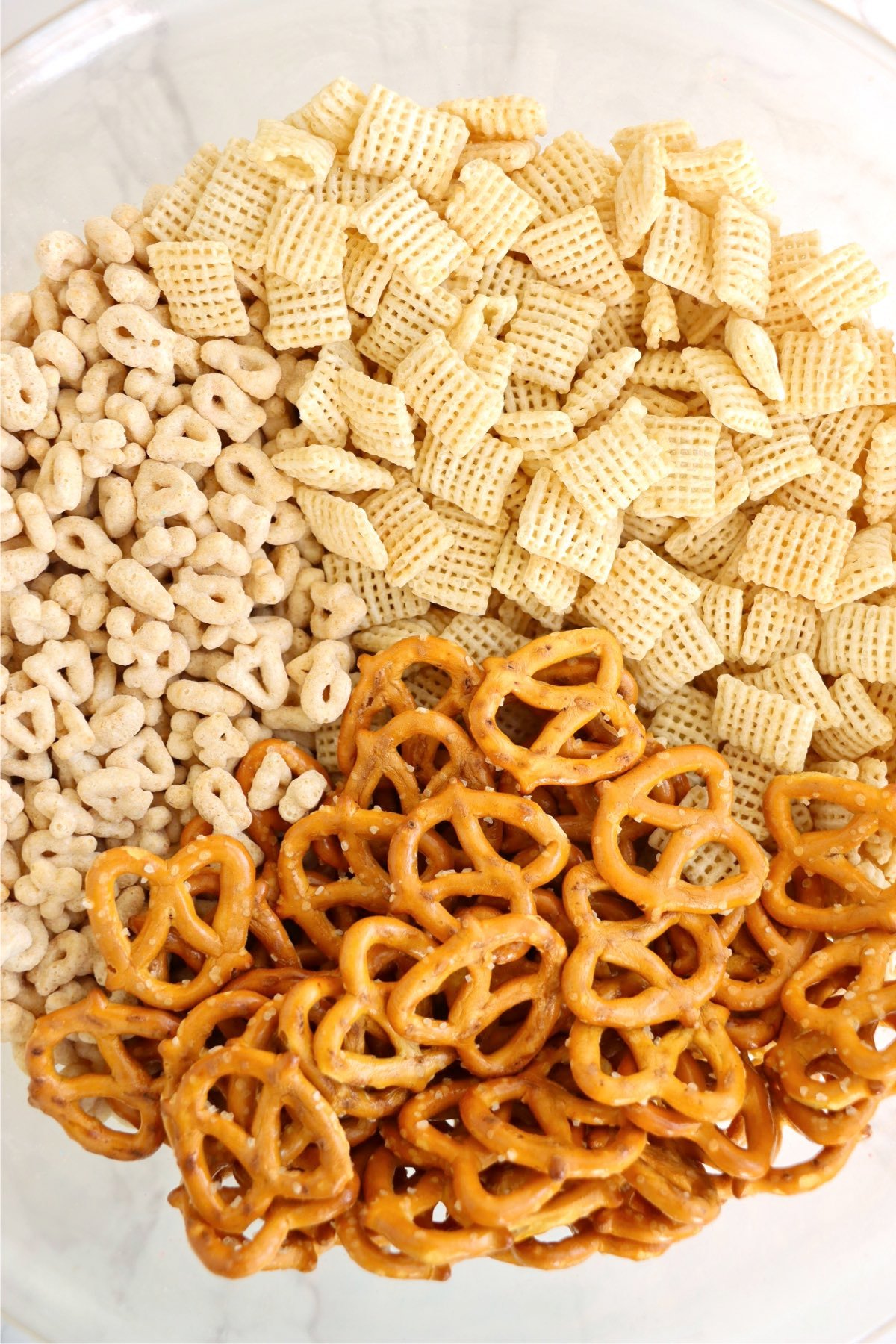 Rice Chex, Lucky Charms cereal, and mini pretzels in a large mixing bowl.