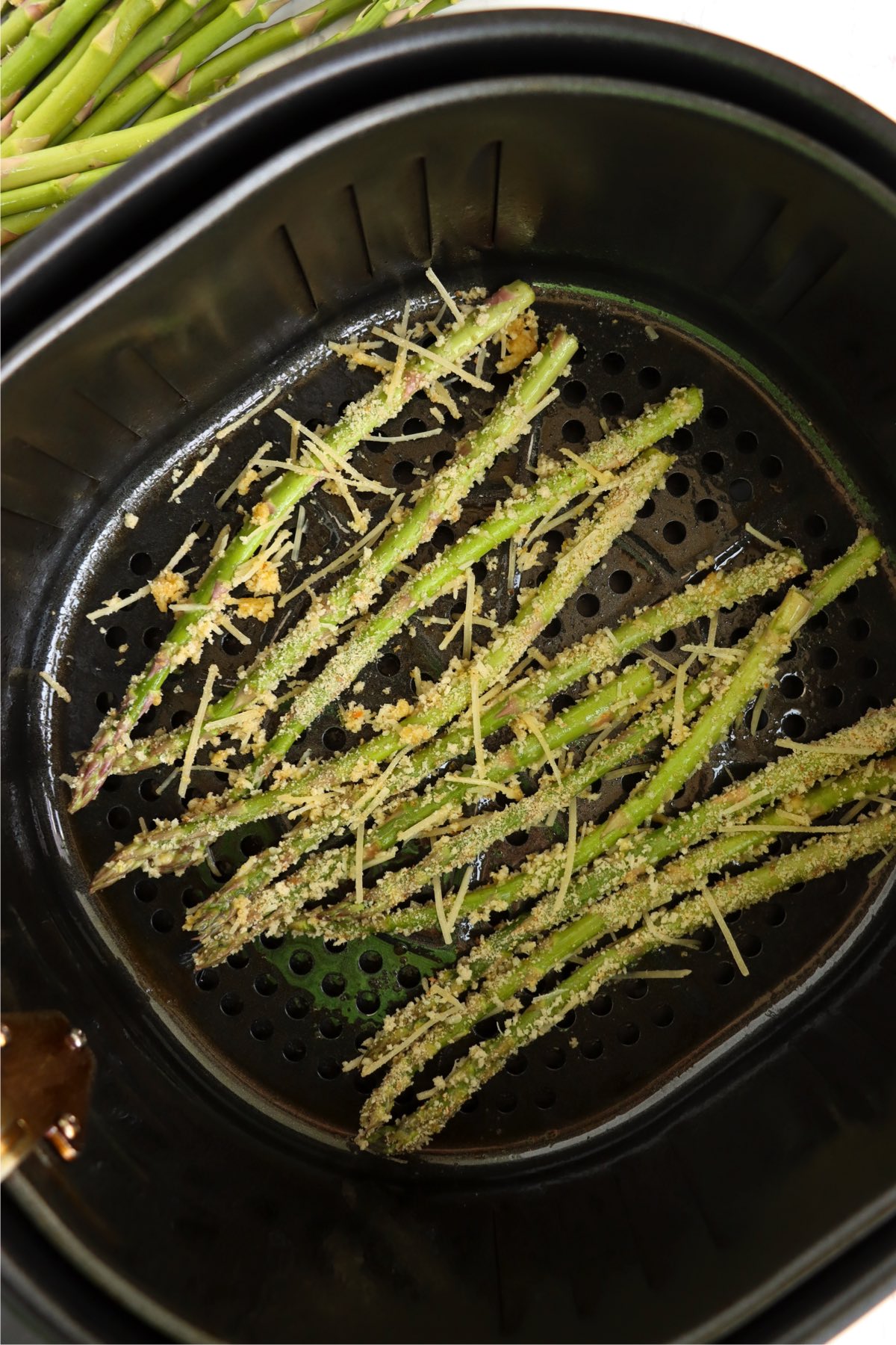 Uncooked breaded asparagus spears arranged in a single layer in the basket of an air fryer, ready to be cooked.