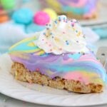 A wide-angle close-up of a pastel swirled dessert slice with rainbow sprinkles and whipped cream, sitting on a plate.