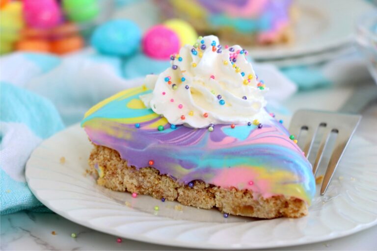 A wide-angle close-up of a pastel swirled dessert slice with rainbow sprinkles and whipped cream, sitting on a plate.