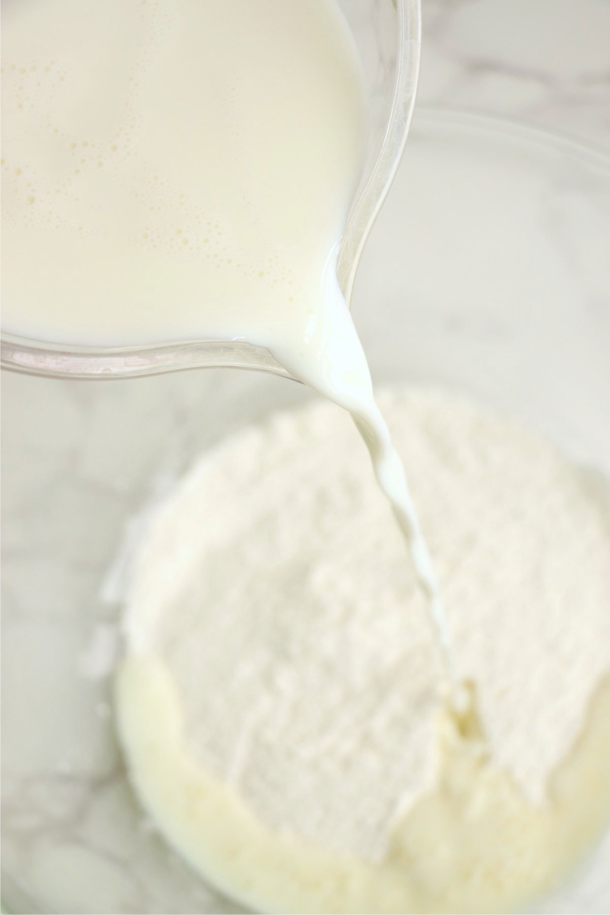 Milk being poured into banana pudding mix in a clear bowl to begin preparing the creamy pudding layer.