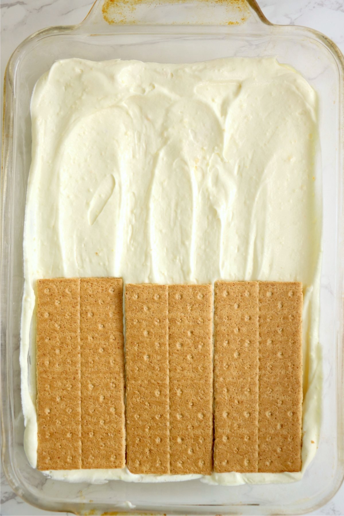 Second layer of graham crackers added over a pudding mixture, showing a layering process.