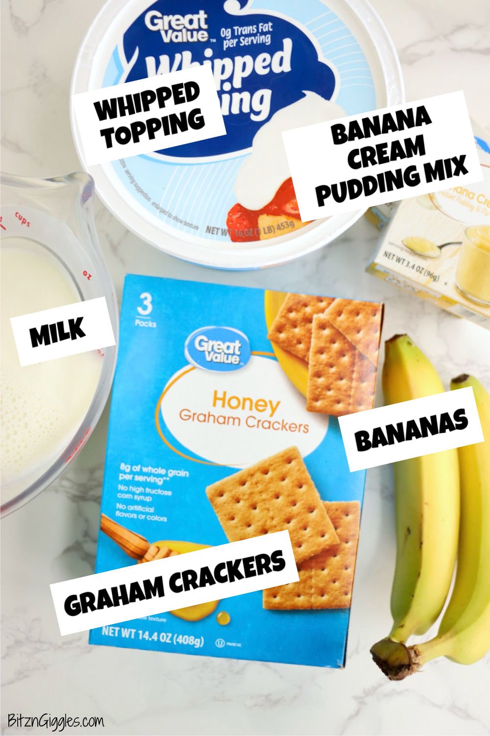Whipped topping, banana cream pudding mix, graham crackers, fresh bananas, and milk laid out on a white table.