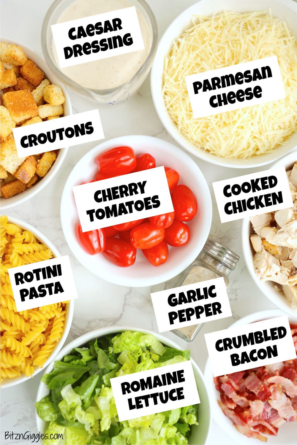 Overhead view of Caesar pasta salad ingredients in separate bowls, including dressing, cheese, croutons, tomatoes, pasta, chicken, lettuce, bacon, and seasoning.