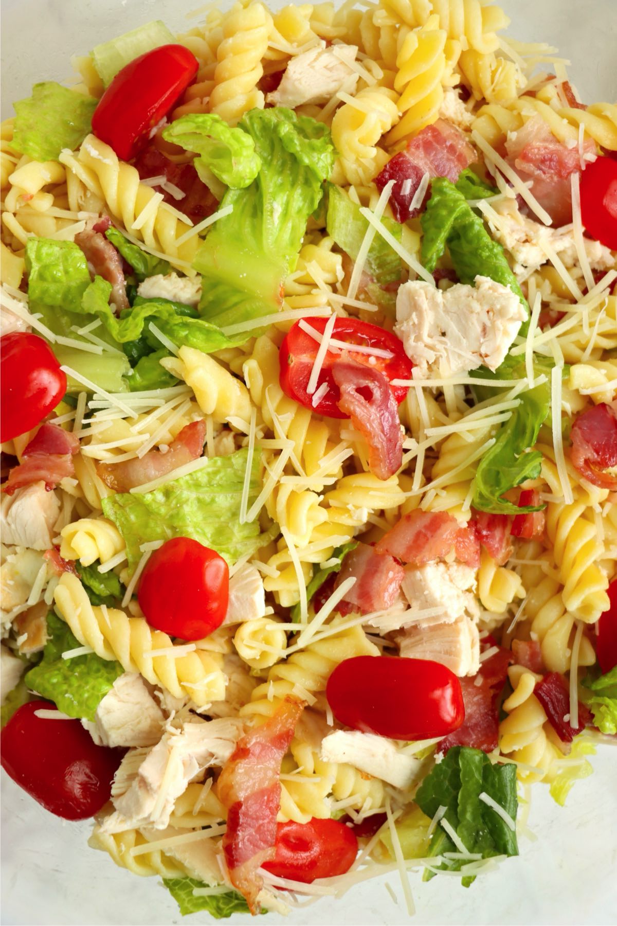Close-up of the pasta salad ingredients mixed together, showing rotini, lettuce, chicken, bacon, tomatoes, and shredded parmesan.