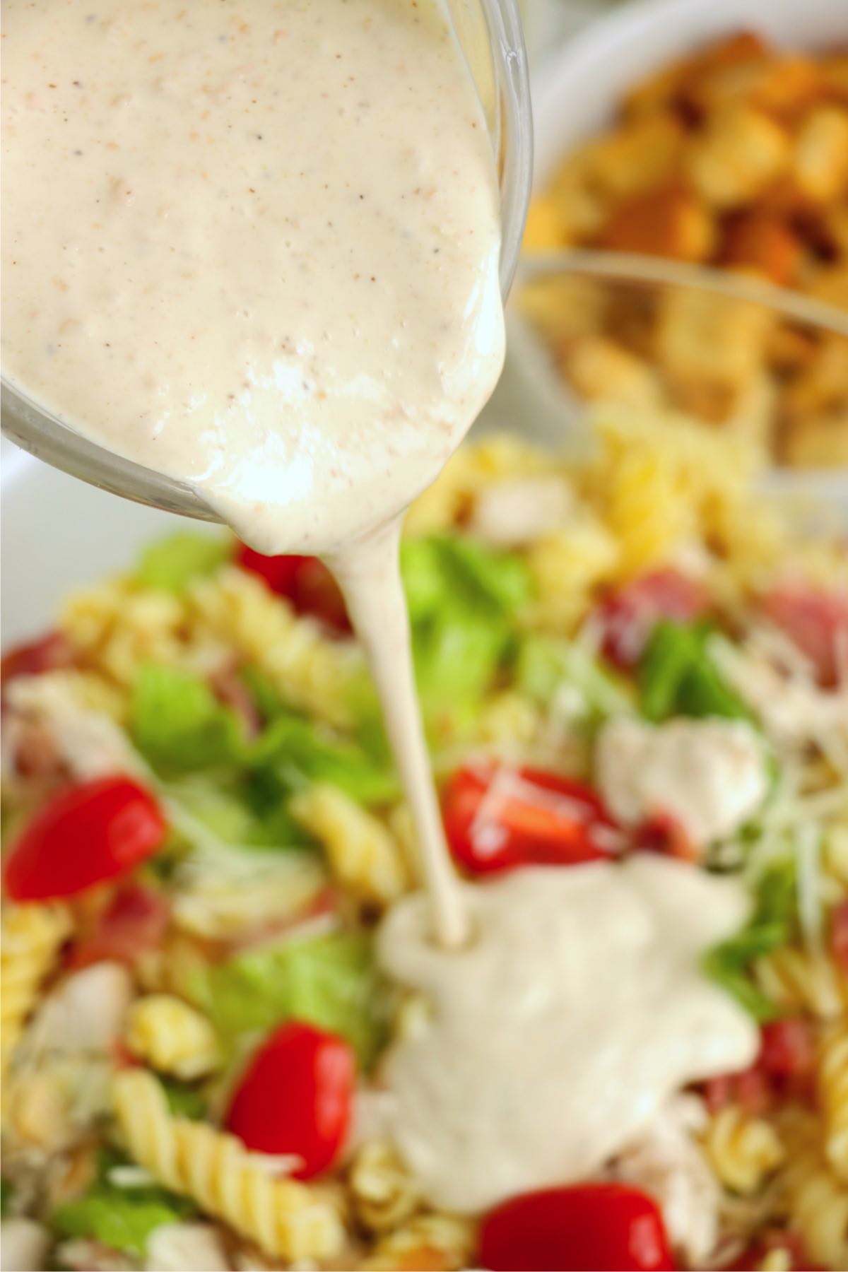 Caesar dressing being poured over the top of the salad ingredients in a bowl.