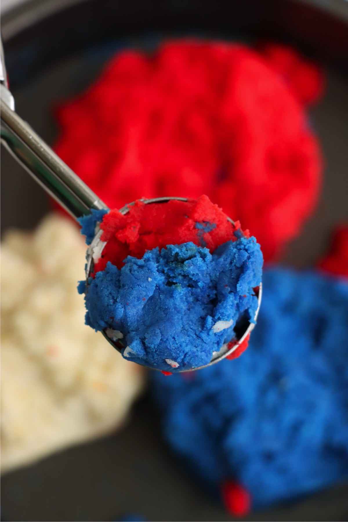Cookie scoop picking up a mix of red, white, and blue cake dough.