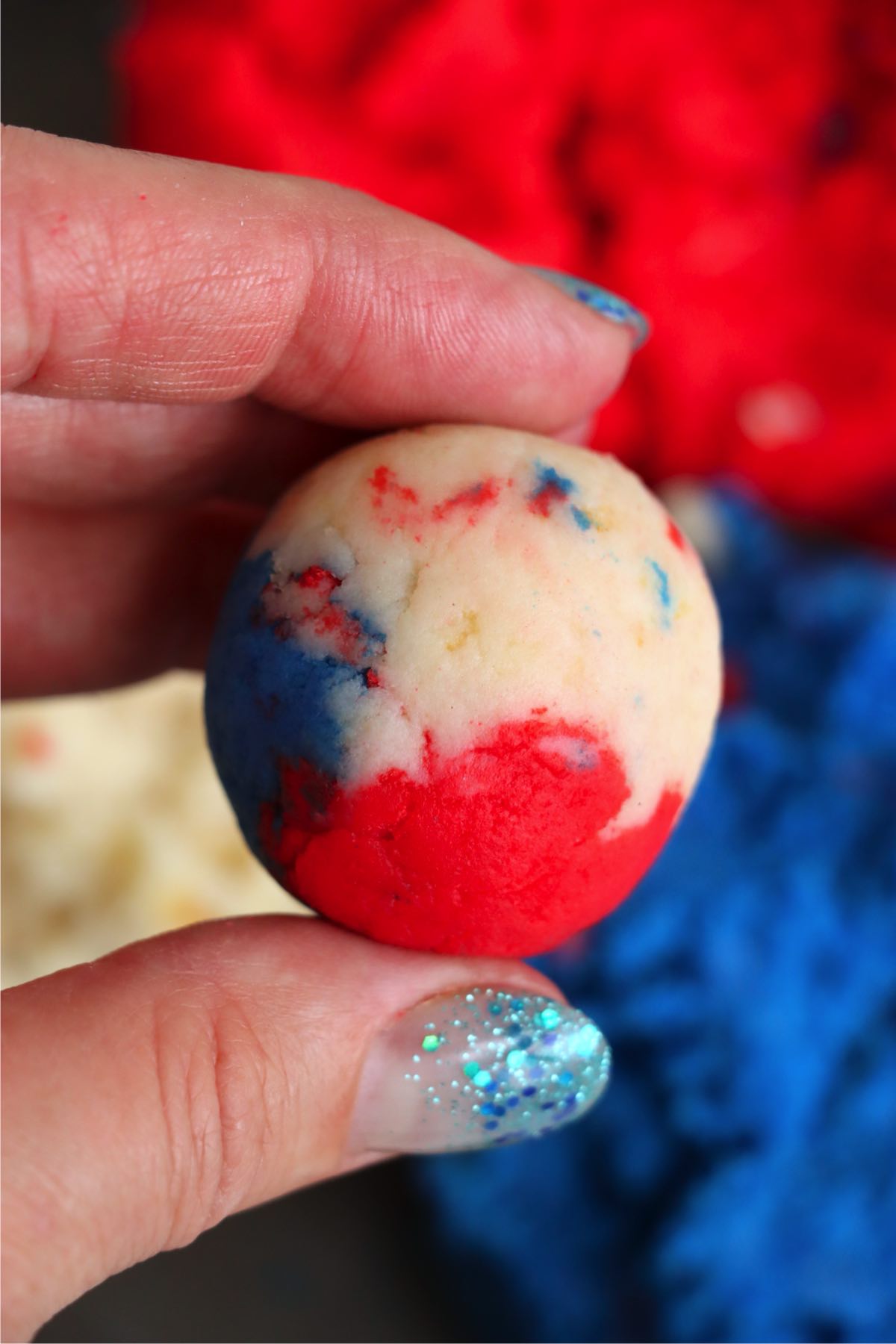 Hand holding a rolled cake pop ball showing red, white, and blue swirls.