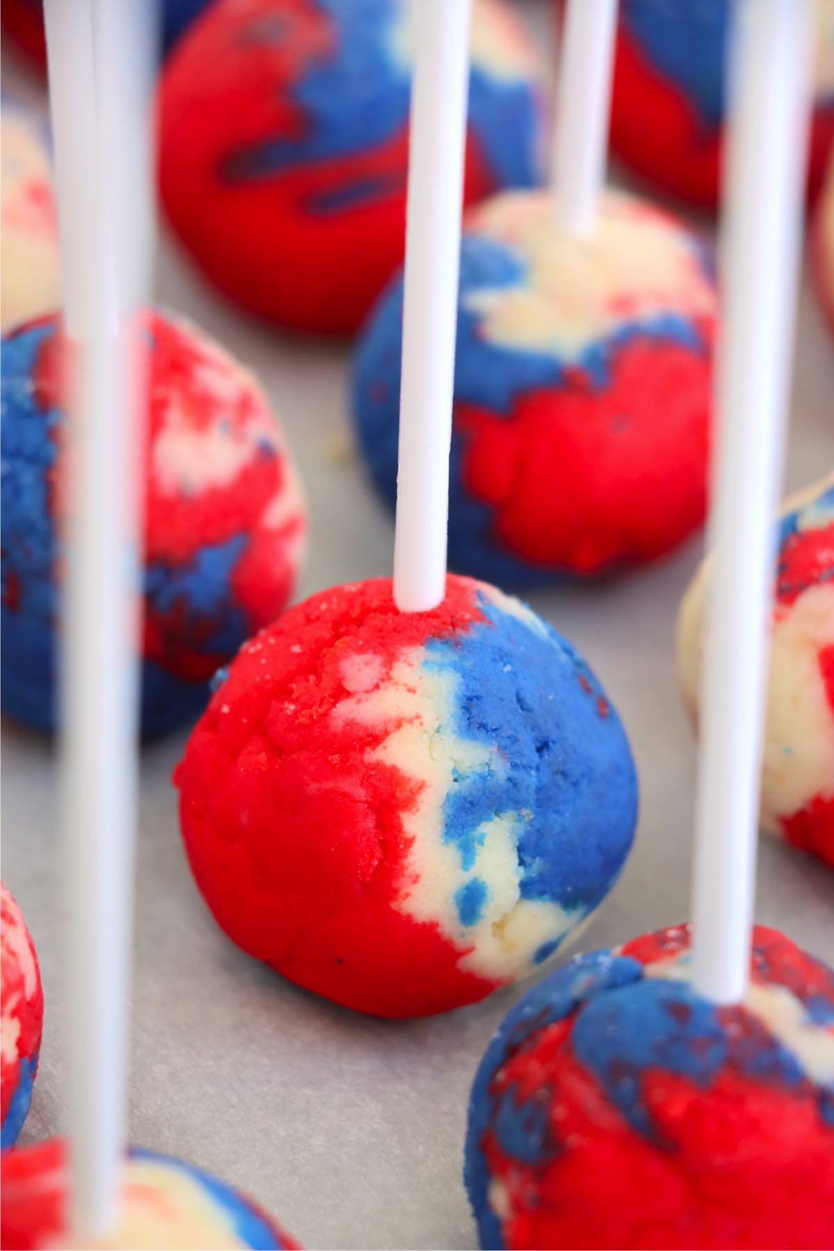 Swirled red, white, and blue cake pops on sticks before dipping.