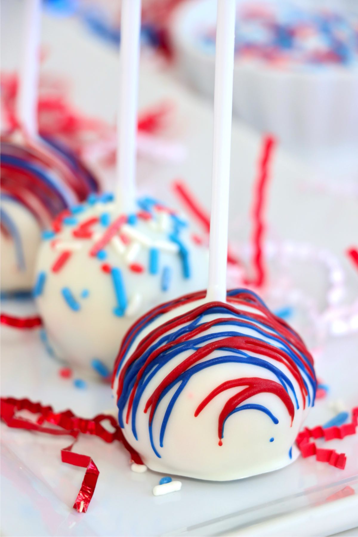 White chocolate-coated cake pops topped with festive red and blue drizzle and sprinkles.