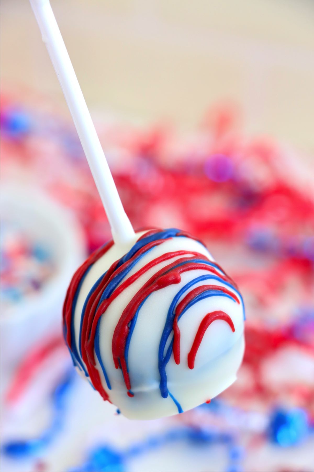One fully decorated cake pop held above the tray with red and blue drizzle.