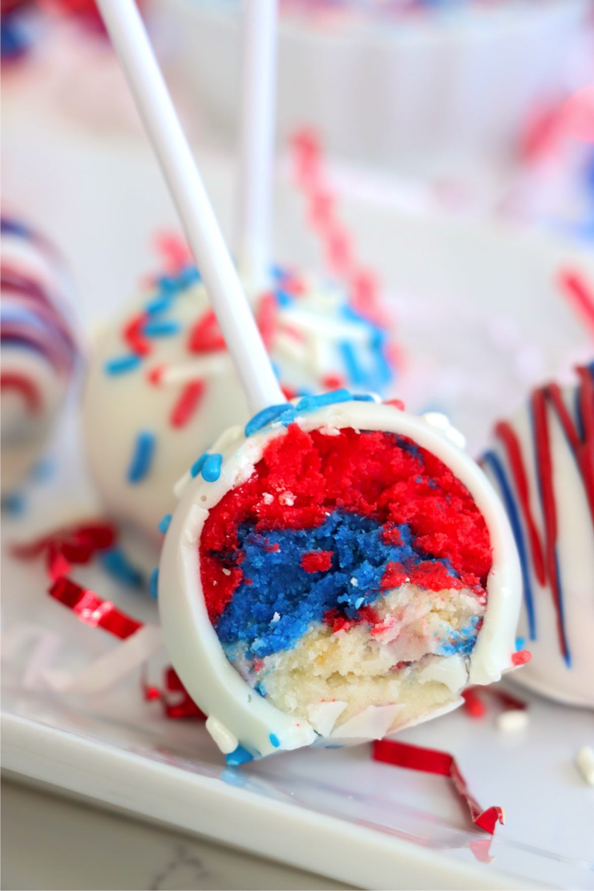 Bitten cake pop revealing vibrant red, white, and blue cake layers inside.