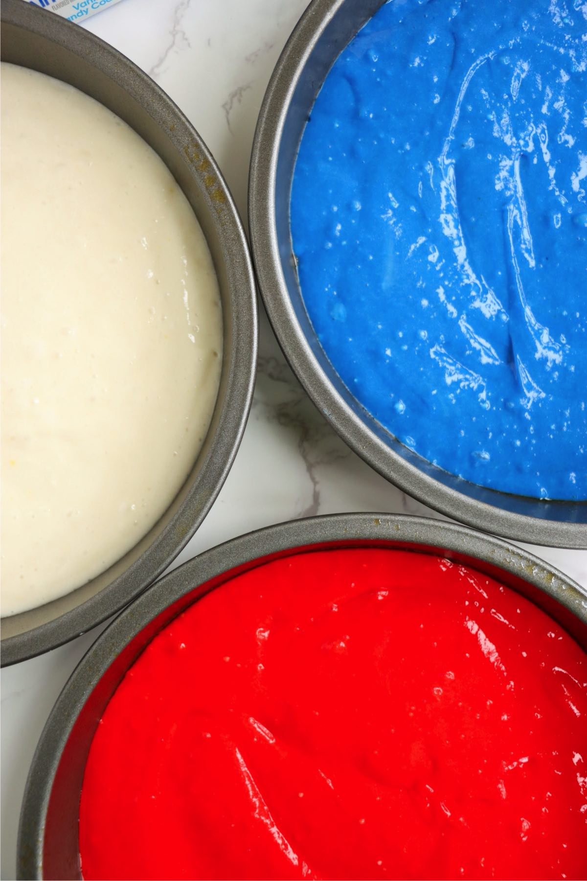 Red, white, and blue cake batter divided into three round cake pans.