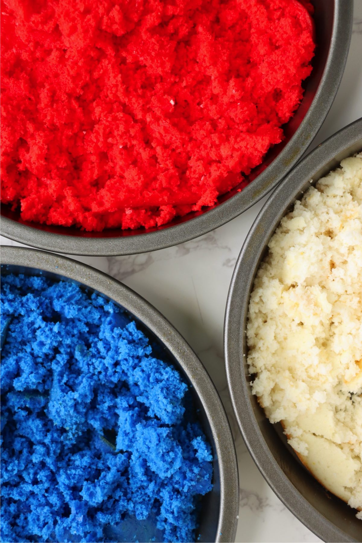 Red, white, and blue cakes crumbled into fine crumbs in round pans.