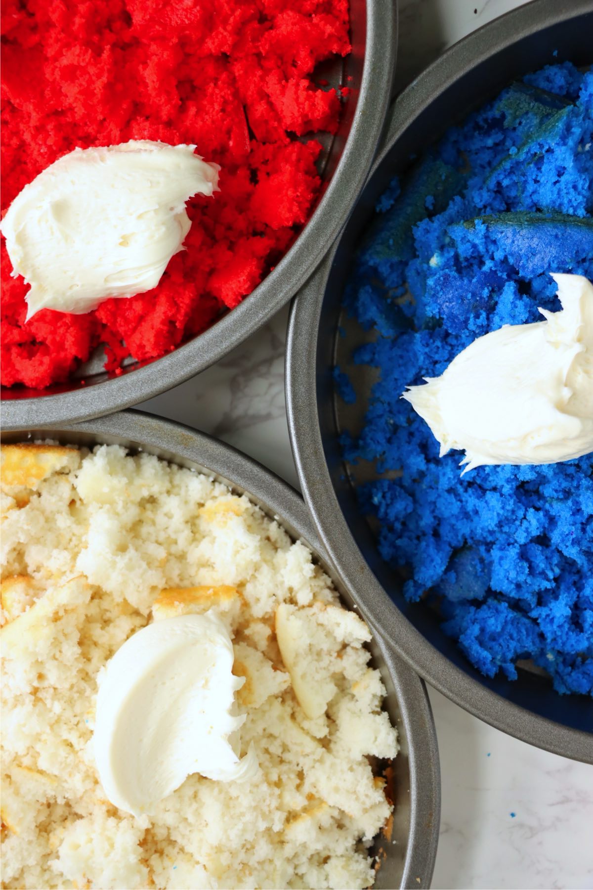 Vanilla frosting added to red, white, and blue cake crumbs for mixing.