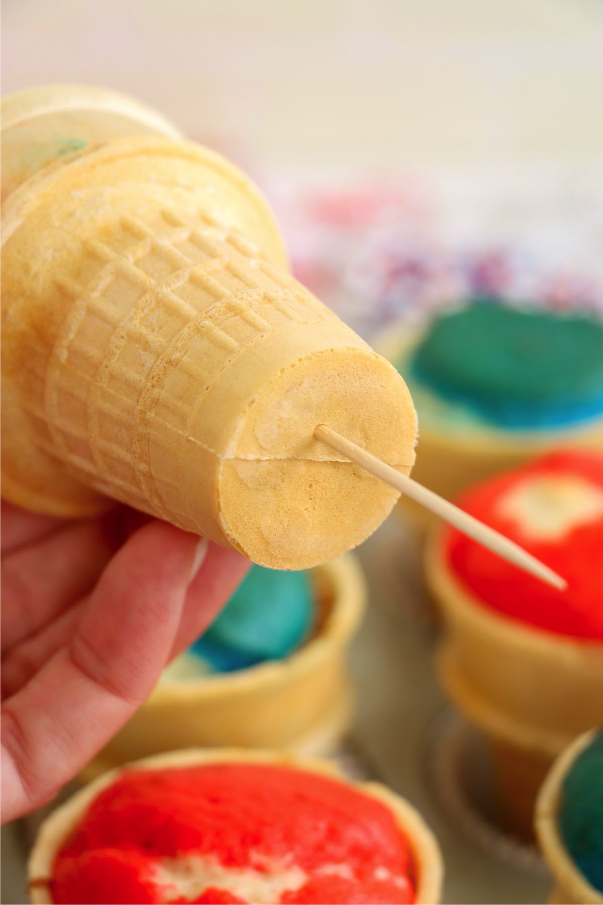 A hand using a toothpick to poke a hole in the bottom of a baked cupcake cone.